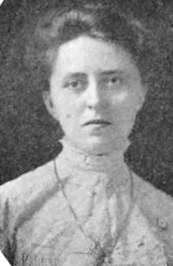A white woman with dark hair, wearing a high-collared blouse or dress. She is not smiling.