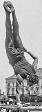 Black and white photo of an upside-down man with one hand on a bar and his other hand on his leg