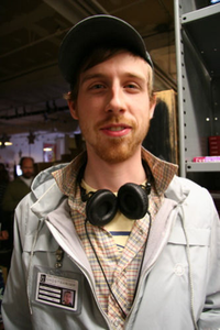 A smiling, squinting Ghostshrimp, in a white jacket with headphones around his neck