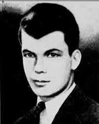 A black and white photo of a young man with well-coiffed dark hair wearing a jacket and tie