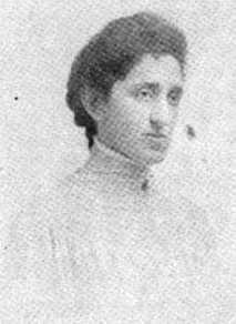 A woman with thick dark hair dressed back into braids at the nape; she is wearing a high-collared white lace shirtwaist or dress.