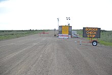 an electronic sign that says "Border Check Stop" on a gravel road.