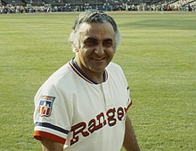 A man in a white baseball uniform with "Rangers" on the chest in red