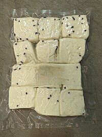 White nabulsi cheese studded with black caraway seeds in a vacuum-sealed package.