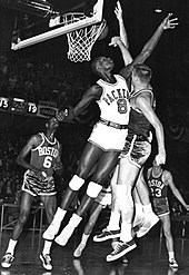 Two players jumping up to shoot and block with others around them