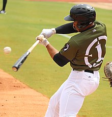 A man in an olive drab baseball jersey and white pants