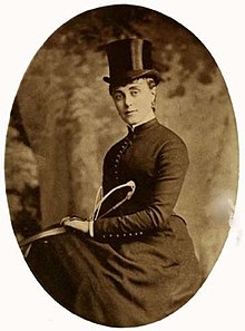 sepia toned photograph of a woman wearing a riding dress and top hat