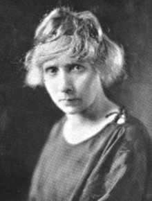 A white woman with tousled fair hair and a stern expression