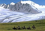 People on horses and camels riding, a snow-covered mountain in the background