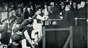 A football player receiving a football cup from a monarch