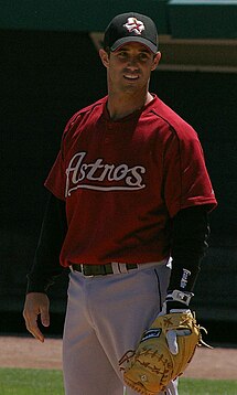 A man in a red baseball uniform stands and looks towards his left.