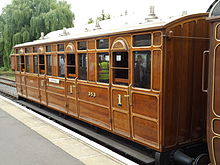 Side view of a varnished wooden railway carriage with doors and windows at regular intervals down the side.