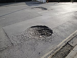 Example of a pothole reappearing on a newly patched roadway, also showing the transition between crocodile cracking and the pothole, with water dried up, in a road on the Isle of Wight