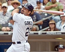 A man in a white baseball uniform and dark batting helmet takes a left-handed swing with a baseball bat in his hands.