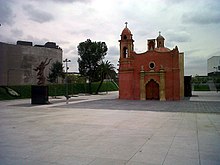 Picture of a square which features two major elements. First, a bronze statue to the left and a small red baroque-style church.