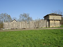 A wooden stockade fronted by a wall of vertically placed logs and a corner blockhouse
