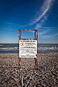 A white sign attached to a wooden structure indicating to patrons on a beach. "No Lifeguard On Duty, Call 911 in case of emergency"
