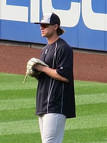 A man in gray pants, black shirt, and black and white baseball cap