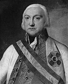 Black and white portrait of a white-haired man with a solemn look. He wears a white military uniform with embroidery on the lapels and a sash.