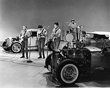The Beach Boys performing, flanked by muscle cars