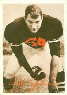Bob Johnson bending over towards the camera with a football in one hand and the other hand on the ground. Wearing a Bengals uniform but no helmet.