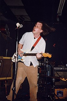 Photo of a man holding a guitar with a microphone nearby