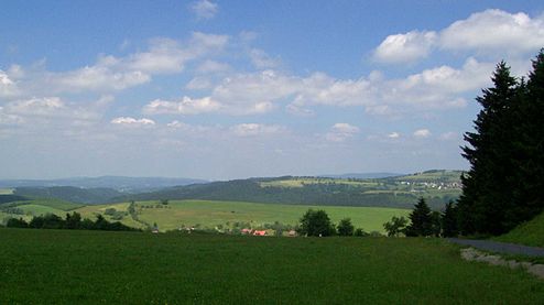 View from the Eckartsberg of Schnett and the Simmersberg (781 m, right) with its subpeak, the Kohlberg (718 m, centre). Between them in the background can be seen the Adlersberg (849,9 m) with the Neuhäuser Hügel (891 m). Left of the Kohlberg in the background is the trading estate of Suhl-Friedberg and the Little Thuringian Forest with the Schleusinger Berg (671 m) and Schneeberg (692 m). Front centre is the village of Waffenrod/Hinterrod.