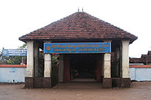 Entrance to low building with four white columns, triangular roof and blue sign