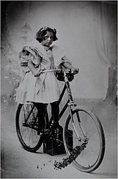 A girl wearing a dress and standing on a bicycle