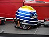 A black carbon fibre HANS device attached to the back of a racing helmet on a helmet anchor