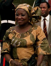 A woman in a yellow and green African-style dress smiles