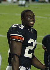 A football player in a black uniform stands on the field.