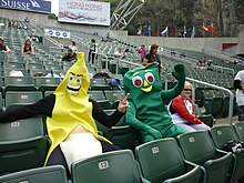 Two people dressed in fancy costume (Gumby – right; Banana – left) seated in stadium