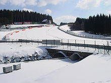 The bridge where the Circuit de Spa-Francorchamps crosses the Eau Rouge stream is located at the corner bearing its name. The right-hand turn visible in the background leading up the hill is Raidillon.[1]