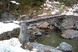 Log bridge in France with dry set stone abutments and a footpath leveled with boards