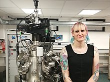 Barker standing in a laboratory, next to a large pulsed laser deposition tool.
