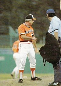 A man in an orange baseball jersey and white pants on a baseball field