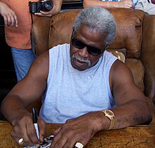 Earl Campbell in a grey sleeveless shiort and sun glasses signing articles.