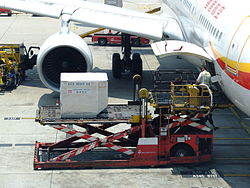 A ULD loader lifting a unit load device (ULD) from apron dollies to an aircraft's cargo bay