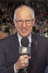 Mike Emrick smiling while holding a microphone in his right hand