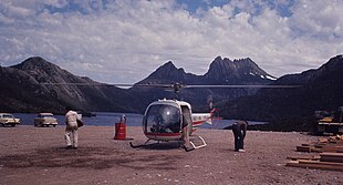 Helicopter and two people, with mountains in the background