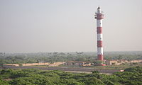 lighthouse with small houses and greenery in the background