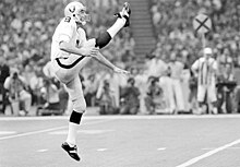 Ray Guy in a Raiders uniform and helmet, punting on the field during Super Bowl XV.