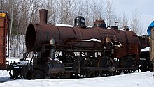 A disassembled steam locomotive with a 4-6-0 wheel arrangement (four leading wheels, six driving wheels, and no trailing wheels) and without a cab sitting outdoors