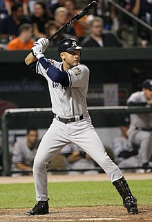 A man in a grey baseball uniform with a navy helmet prepares to swing at a pitch.