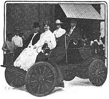 An automobile with four passengers in 1904, including a woman in a long white dress in front.