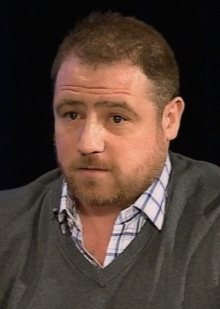 A 39-year-old man with a brown buzz cut and a beard looking to the left of the camera.