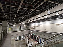 A black-and-white calligraphic mural on the wall above the station platforms. There are escalators, lifts and stairs leading from the concourse to the platforms.
