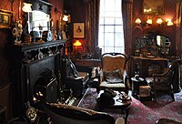 Cluttered room with fireplace, three armchairs and a violin