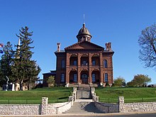 The Washington County Courthouse is a red brick building. Atop the building is a dome with multiple windows. There is a staircase leading up to the courthouse entrance. The entrance sits under an archway and consists of two wooden doors.